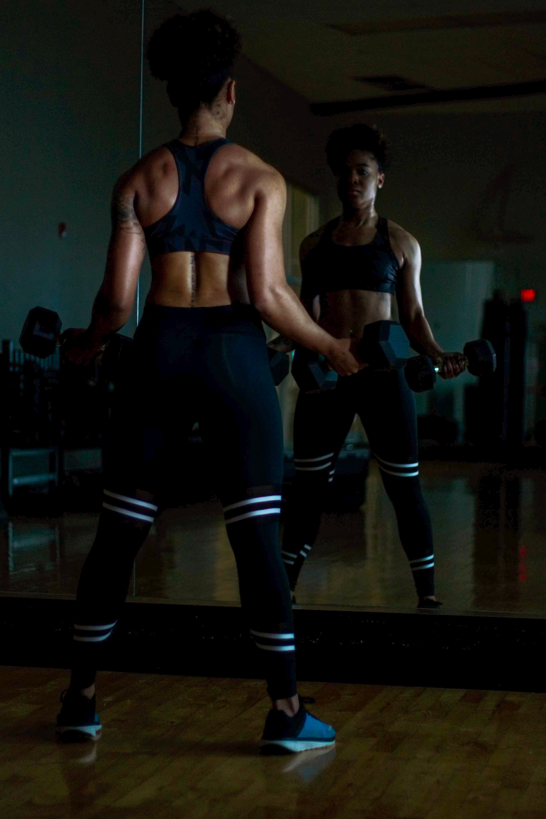 Woman Lifting Two Dumbells on Both Hands in Front of Mirror